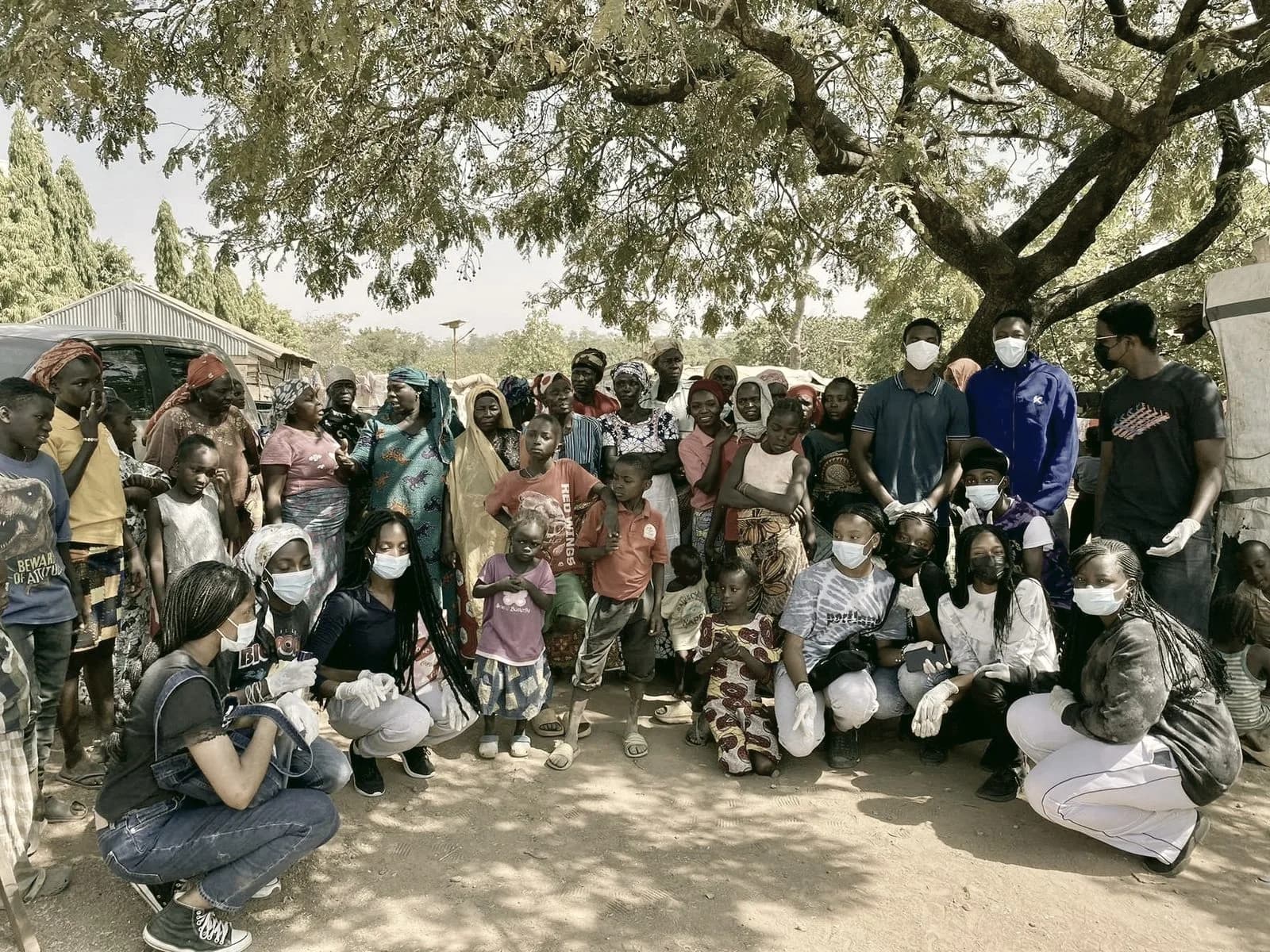 Community members and volunteers gathered together under a large tree at an Abuja IDP camp