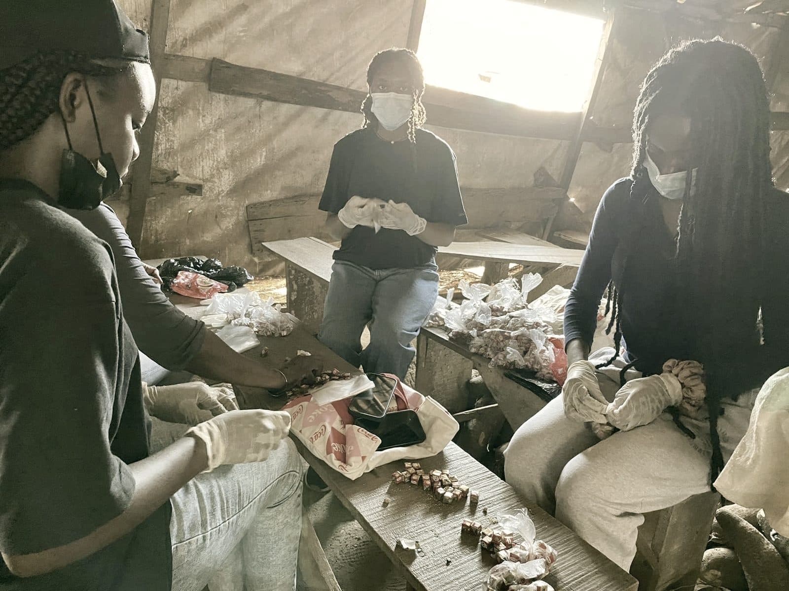 Volunteers seated on wooden benches packing seasoning cubes and supplies into small bags