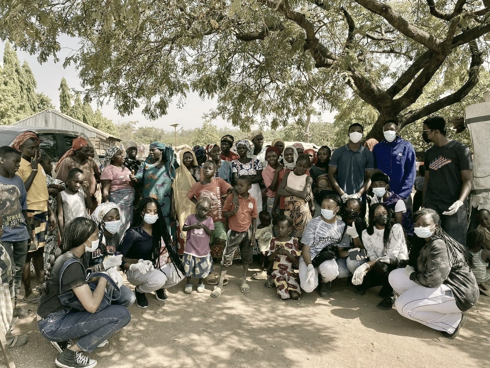 Community members and volunteers gathered together under a large tree at an Abuja IDP camp