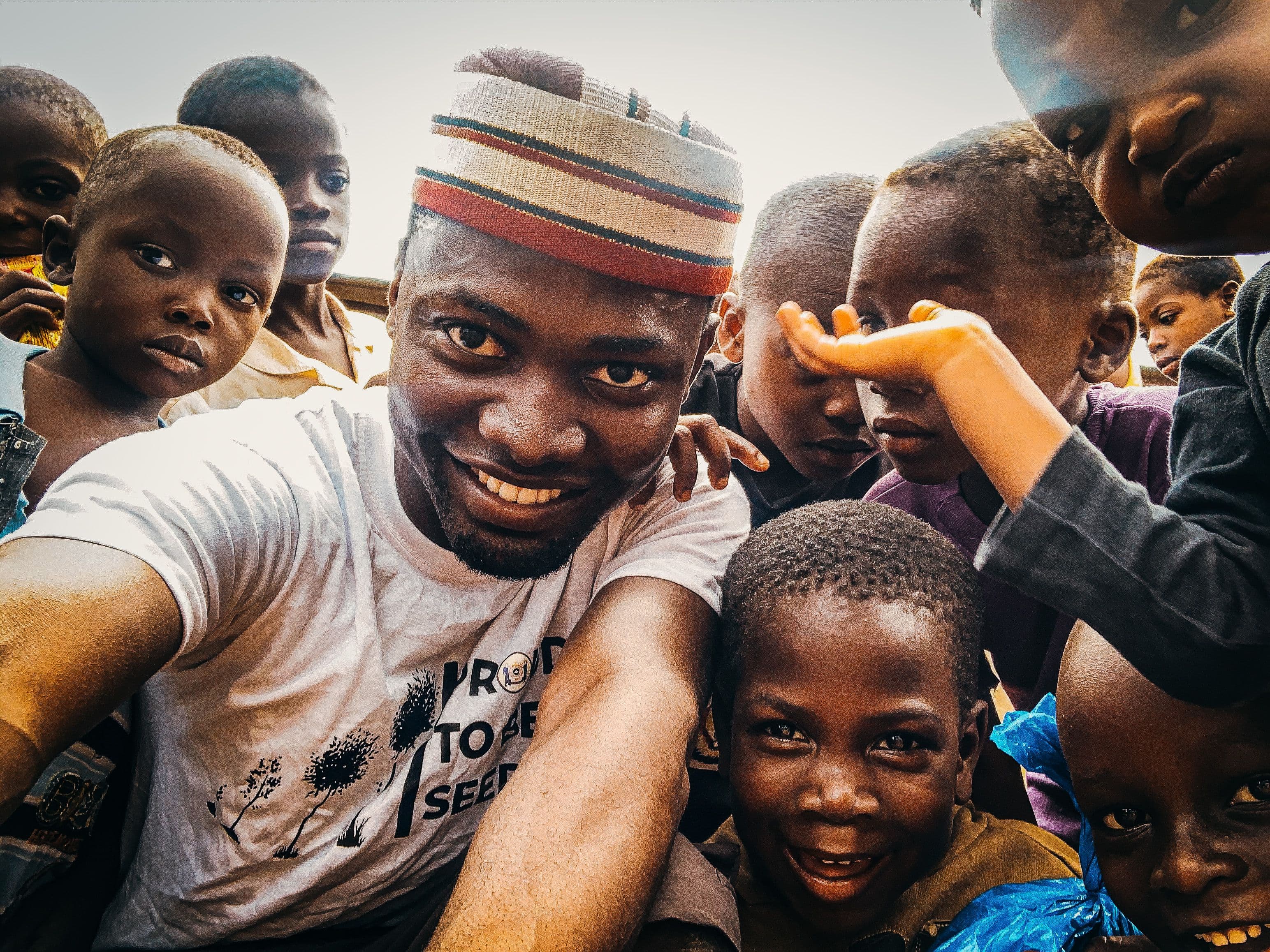 A man in a patterned cap and a close group of children look toward the camera