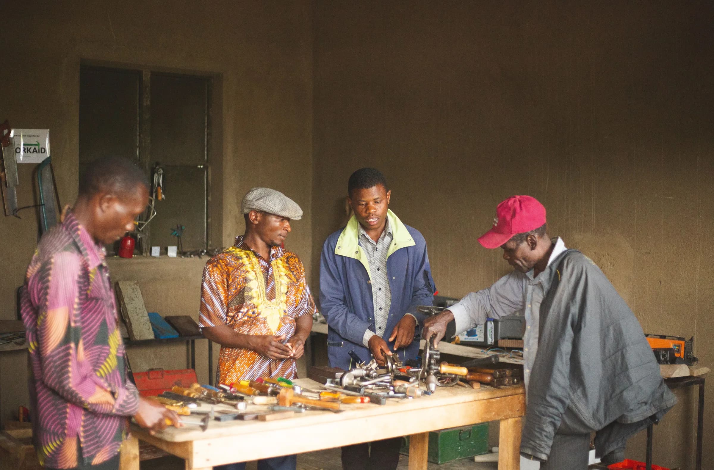 Four men gathered around hand tools and equipment at a workshop bench